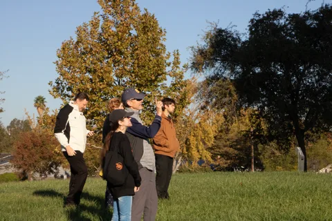 A small group walks together across the open field beneath scattered trees.