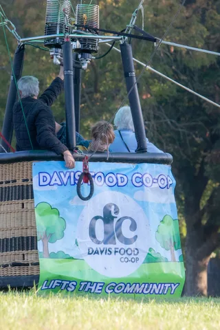 The balloon basket hangs against the sky, wrapped in its Davis Food Co-op banner.