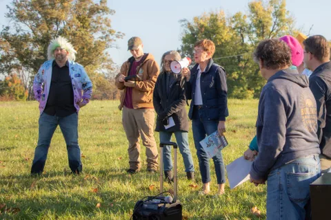 A small group stands together in the grass, one holding a megaphone.