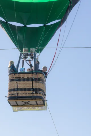 Two riders are silhouetted against the bright sky inside a hot air balloon basket.