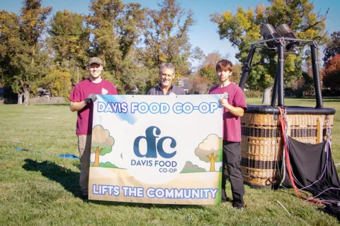A group poses with the Davis Food Co-op banner between two balloon baskets.