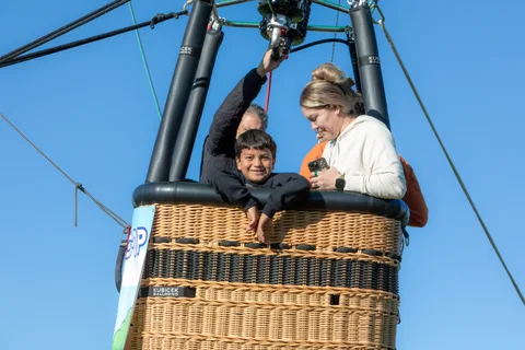 A woman reaches up excitedly beside a man in a cap while a boy looks on in the basket.