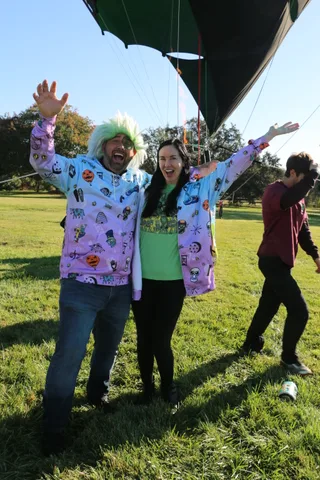 A couple throws their arms up celebrating on the grass at the balloon field.