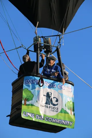 The balloon basket with the co-op banner rises past the treeline.