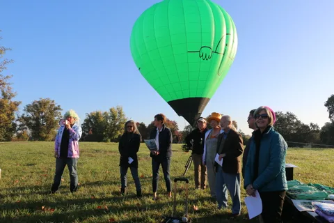 The green balloon fills the sky above a crowd gathered to watch it rise.