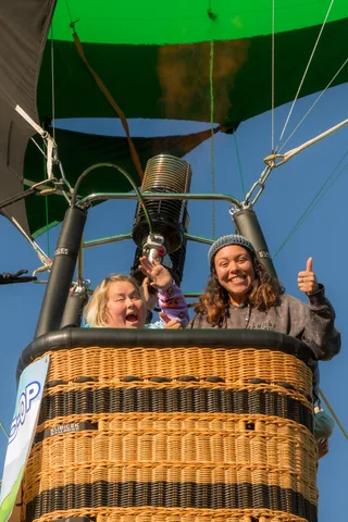 Two women in the balloon basket burst into unguarded laughter and mid-air excitement.