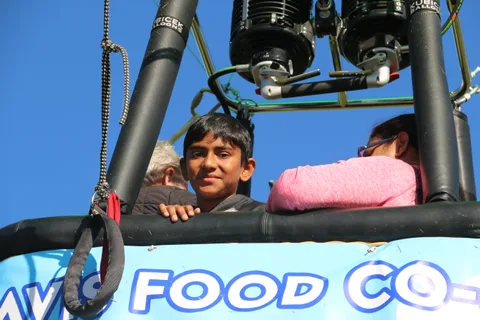 A boy smiles from the balloon basket with a girl in pink beside him.
