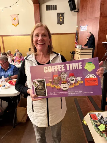 A raffle winner holds up the Coffee Time board game and an Upper Crust Baking gift card.