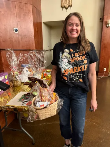 A raffle winner holds a wrapped gift basket beside the prize table at the lodge.