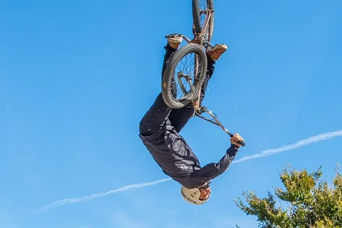 A BMX rider is caught upside down mid-trick against a clear blue sky.