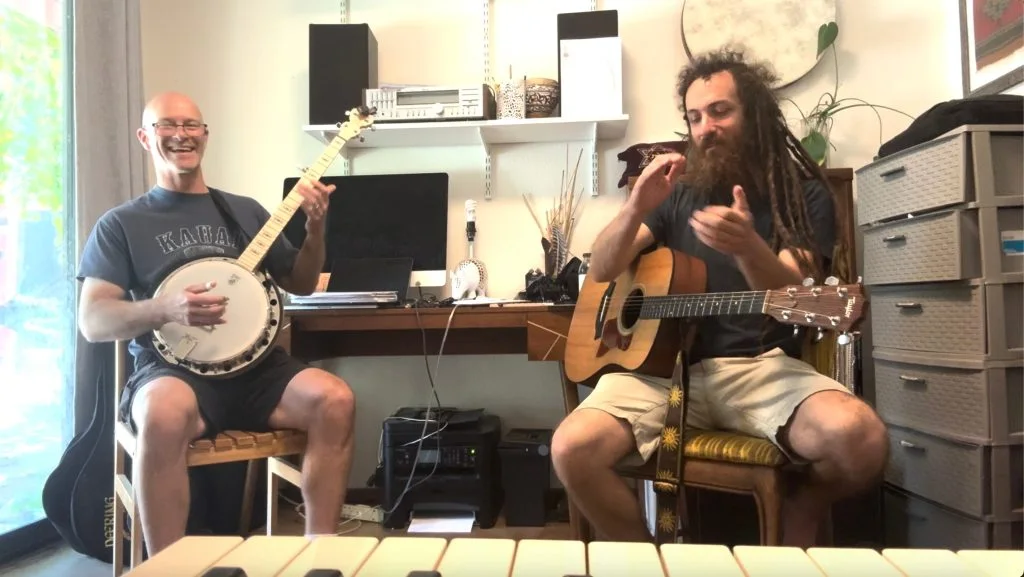 Two musicians playing together at PlayReady Music, one on banjo and one on guitar, mid-song and smiling.
