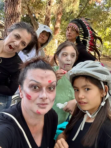 A group of friends in zombie makeup gathers close for a candid selfie at the park.