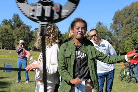 A young woman smiles and reaches out at a festival ring-light photo booth.