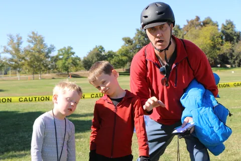 A costumed man crouches to talk with two young boys near the bike course.
