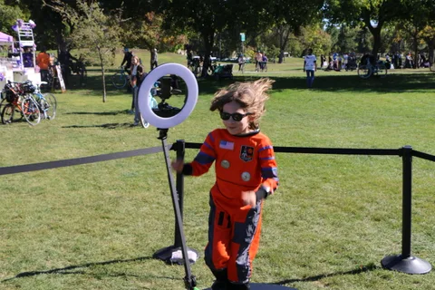 A kid in an astronaut costume and sunglasses flips his hair by the photo booth.