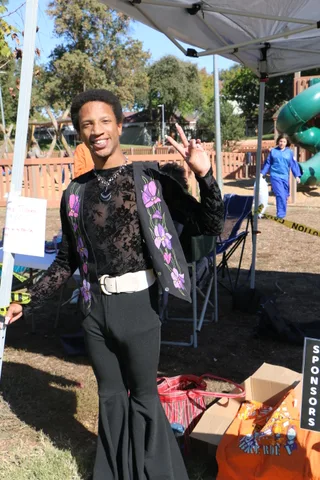 A costumed young man waves under a shaded festival tent.