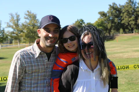A man poses with two costumed companions smiling for the camera.