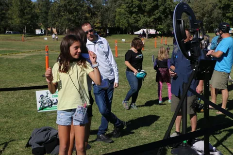 A girl dances past festival photo booth equipment on the grass.