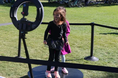 A girl stands on a photo booth platform surrounded by ring light equipment.
