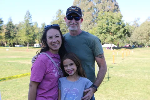 A family of three smiles together outdoors at the festival.