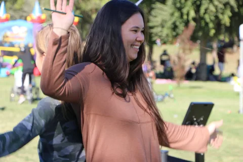 A woman laughs and waves while dancing at the photo booth, bounce house behind her.