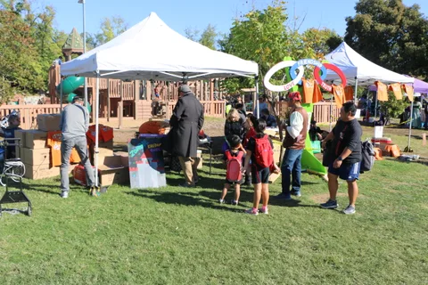 Kids play a ring toss game near a tent in the park.