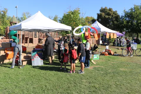 Families gather near a tent with games set up in the park.