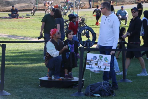 A father and daughter in costume stand on a photo booth turntable in front of a 360 Zombie Videos sign.