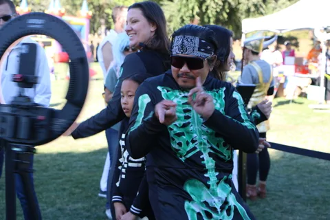 A man in teal skeleton body paint points playfully at the camera with a child nearby.