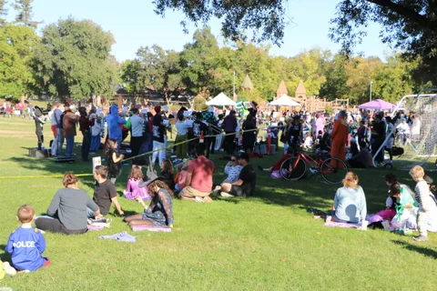 A large crowd gathers across the park near vendor tents.