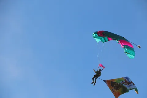 A skydiver unfurls a colorful streamer flag while descending under canopy.