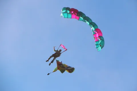 A skydiver holding a banner falls beneath two parachutes crossing overhead.