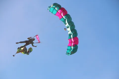 A skydiver flies a flag banner sideways beneath an open parachute.