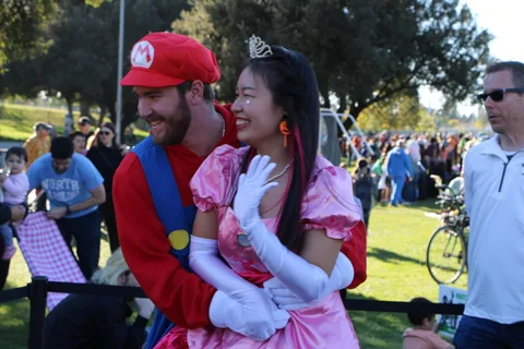 A costumed couple dressed as Mario and Princess Peach laugh together in the crowd.