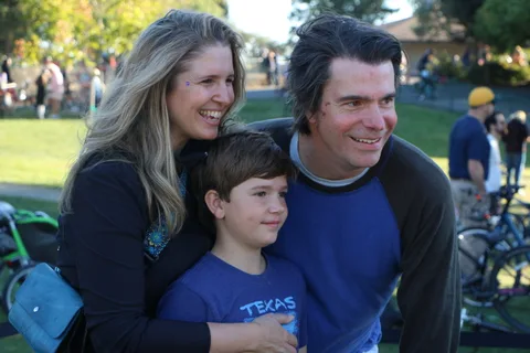 A mother and father smile with their son, who wears a Texas shirt.