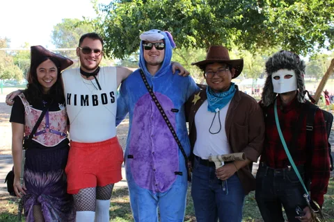 Four friends in costume, including a cowboy and a wolf onesie, pose together smiling.