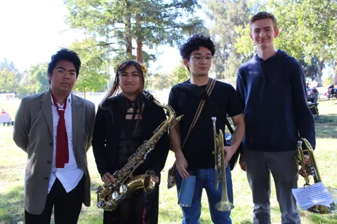 Four young musicians pose with a saxophone and trumpets on the park lawn.
