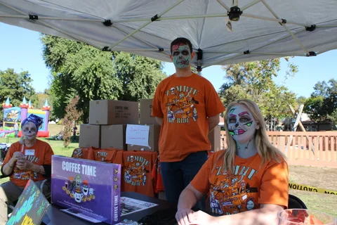 Volunteers in zombie makeup and orange event shirts staff the Coffee Time board game booth.