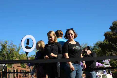Three women pose together near a ring light stand under a clear sky.