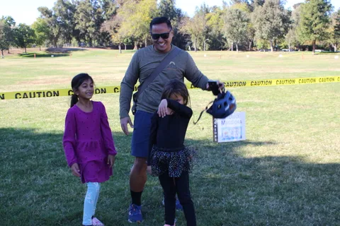 A father helps his daughter with a helmet on the park lawn.