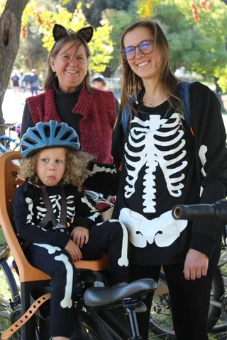 A grandmother in cat ears and a woman in a skeleton costume smile together in the park.