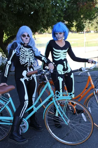 Two riders in blue wigs and skeleton bodysuits pose with their bikes.