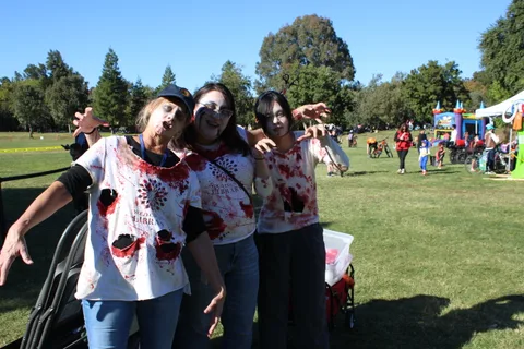 Three friends in bloodstained zombie costumes pose together on the lawn.