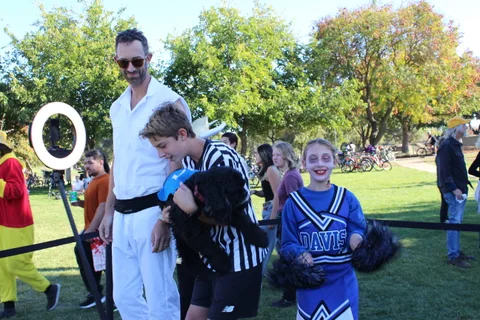 Boys in a ghost costume and referee uniform pose together at the park.