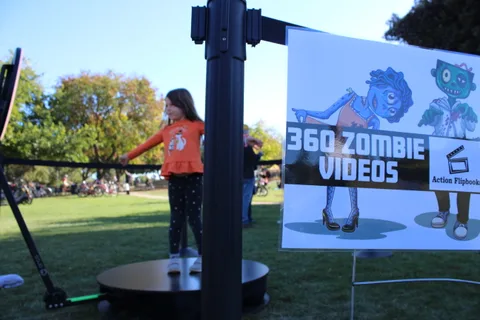 A girl in an orange shirt stands on the 360 Zombie Videos photo booth turntable.