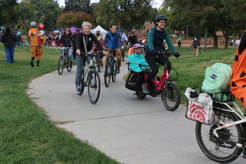 Costumed riders gather with decorated bikes on a park path at the zombie bike parade