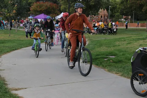 A child in a pink helmet leads a line of costumed riders along the path.