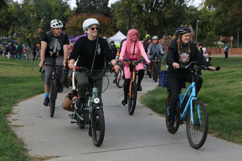 Three costumed riders approach on the parade path with a crowd behind them.