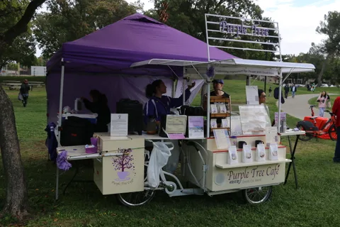 The Purple Tree Cafe cargo-bike coffee cart is set up under a purple tent.