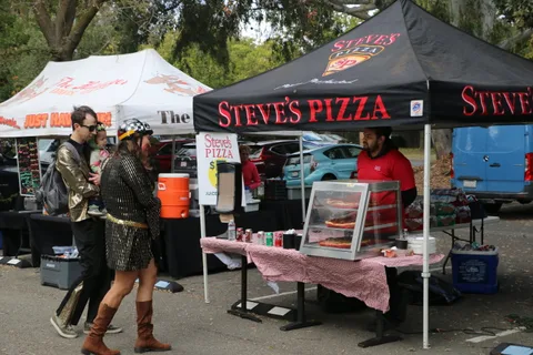 A family in gold costumes walks past the Steve's Pizza vendor tent.